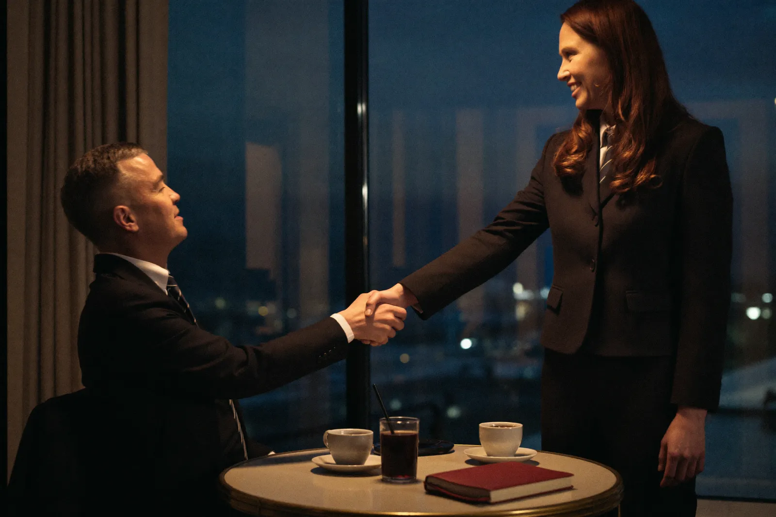 Two business owners shaking hands at a table by a window